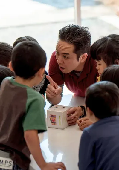 AES英会話のレッスンで先生と子どもたちがテーブルを囲んでアクティビティに集中している様子。
