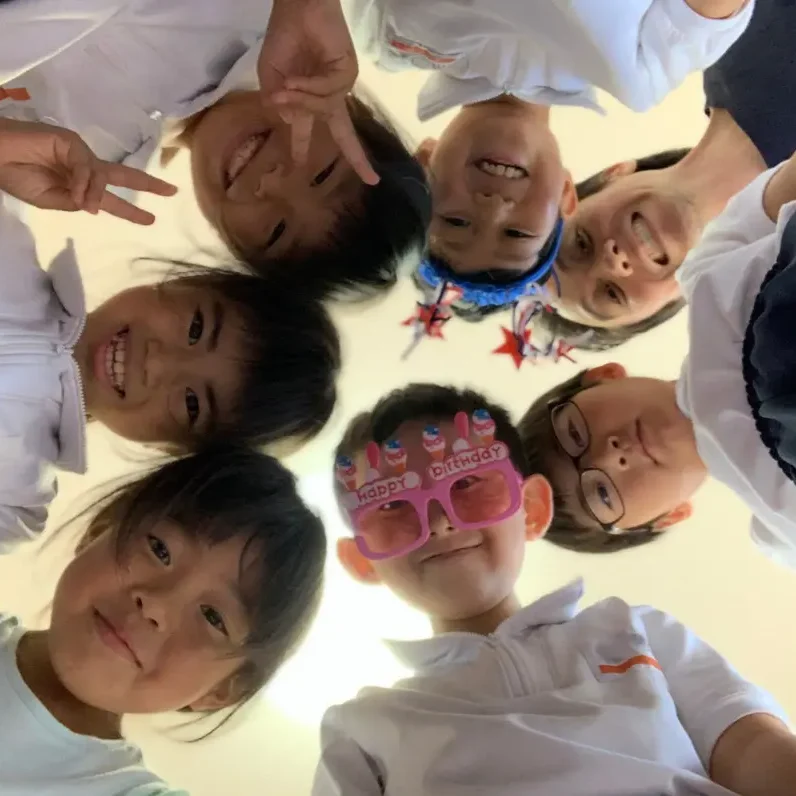 垂井町の英会話教室AESで笑顔の子どもたちが円になって楽しんでいる様子。誕生日パーティーのような雰囲気で、英語を通して自然なコミュニケーションを楽しんでいます。