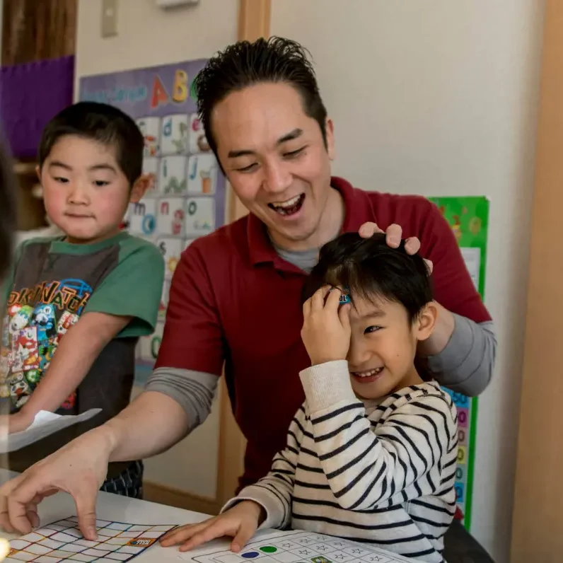 AES英会話のレッスン風景。先生と子どもたちがテーブルでアクティビティを楽しみながら英語を学んでいます。